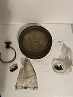 Wide view of the brass clock face with vacuum gauge, clamp ring and bags of small parts laid out on a white background.