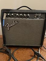 Front view of Fender Frontman 15G amplifier showing control panel, input jack, and Fender logo with attached power and instrument cables.