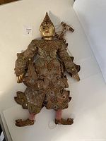 Front view of the Indonesian string puppet, highlighting its ornate fabric, beadwork, and gold coloring on the face and costume.