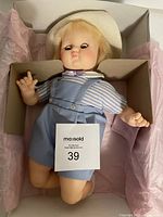 Front and side view of Madame Alexander Baby Brother 4440 doll seated in original box, showing outfit and hat