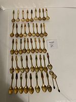 Full view of 46 spoons laid out flat showing gold tone, enamel decorations, and two distinct outliers.