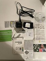 All items included in the lot displayed on a white surface showing the camera, charger, battery, manuals, cable, CD, and camera case.