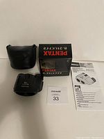 Photo showing binoculars, black soft case, original box with product details, and folded instruction manual.