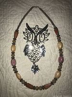 Photo showing the black and gold enameled owl pendant with diamond-like eyes, placed next to the semi-precious stone necklace.