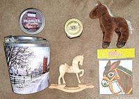 Overhead view of all five items showing the carved wooden rocking horse, stuffed horse, water globe, donkey game, and barnyard tin with cover labeled peanuts (no peanuts included).