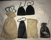Top view of all seven bags laid out on a textured white surface showing various sizes, colors, and materials including burlap, mesh, velvet, satin, nylon, and canvas.