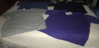 All four plus size women's short sleeve shirts laid out on bed showing colors and condition including new with tags purple shirt and printed B.U.G. shirt