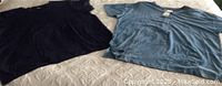 Two women's short sleeve shirts, one solid dark blue textured crew neck and one solid blue with buttons, laid flat on a surface.