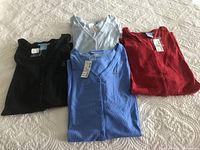 Four folded women's Venezia Jeans buttoned down short sleeve shirts in black, light blue, blue and red laid out on a bedspread, showing the colors and tags.