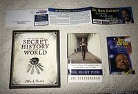 Front covers of the three books arranged on a white surface along with Ben Carson presidential campaign flyers and literature showing the visuals and condition of lot contents.