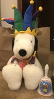 Front view of the Macy's Snoopy plush wearing multicolor jester hat and holding a party horn and tag