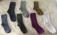 Seven pairs of ankle high socks displayed flat on a surface showing a variety of colors and patterns including solid and polka dots.