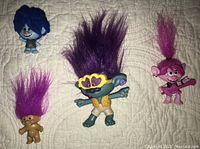 Photo showing four Trolls figures including Russ purple hair troll, Hasbro Dreamworks pink-haired Poppy troll with guitar, McDonald's 2020 purple-haired troll figure, and blue bobble head troll.