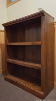 Front view of the wood bookcase showing three shelves and scratches.
