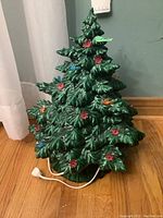 Full view of green ceramic Christmas tree with some colored flower and bird-shaped reflectors attached and power cord visible