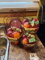 Photo of ceramic canisters in apple shapes with lids, one showing chip on leaf and stem, set on kitchen counter.