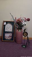 Wood framed wall clock with two clock faces and duck imagery, pink glass vase with an assortment of faux flowers, and metal peacock desk clock on base.