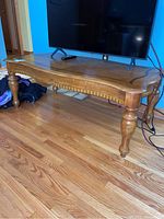 View showing the overall wood coffee table with a TV on top, highlighting turned legs, dental trim, and tabletop shape