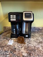 Front view of black and silver Hamilton Beach FlexBrew coffee maker with glass carafe and K-Cup basket on countertop.