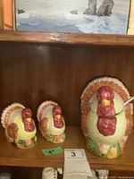 Three ceramic turkey-shaped items displayed on a wooden shelf: two smaller salt and pepper shakers and one larger cranberry dish with spoon.