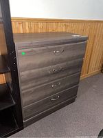 Full view of the wood dresser with four drawers, medium brown finish, placed against a wood panel wall.