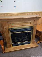 Electric fireplace front view showing wood frame, black and brass metal insert with smokey glass doors and artificial logs inside.