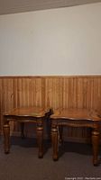 Full view of the two matching wood end tables side by side against a wooden panel wall.