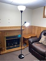 Full view of the black floor lamp standing next to a couch and fireplace in a room.