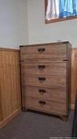 Front view of wooden high boy dresser with five drawers and matte metal handles and corner accents.