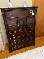 Full front view of dark wood highboy dresser with 8 drawers and small central cupboard door, all having round metal knobs.