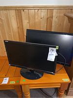 Two monitors stacked on a wooden table, showing the front side of the smaller Sceptre monitor and the back of the larger Asus monitor.