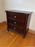 Front view of the wooden night stand showing three drawers with silver round knobs and overall dark brown finish.