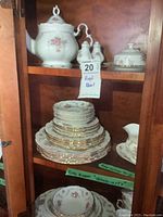 Overall china pieces stacked and displayed in cabinet, showing multiple plates, cups, and serving pieces arranged by size and type.