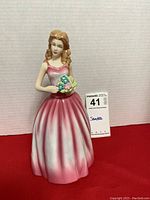 Front view of the Royal Doulton lady figurine "Sandra" showcasing the pink gradient dress and flower bouquet with seller's lot card beside it.
