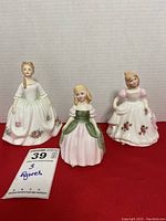 Three Royal Doulton figurines displayed side by side on a red surface with a label showing lot number and quantity.