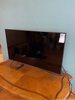Front-right angle of TV on wooden table with remote positioned in front and auction tag visible