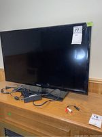 Full frontal view of Samsung 32 inch TV on stand with power adapter and RCA cable on wooden surface.