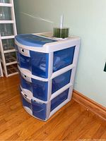 Three drawer plastic storage unit from an angle showing blue semi-transparent drawers and overall design with candle on top.