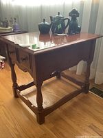 Side view of solid wood end table showing dovetailed drawer and turned legs