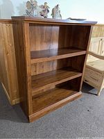Frontal view of solid wood bookcase showing two adjustable shelves and wood grain finish