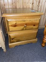 Wood nightstand shown from front displaying two drawers, wooden finish, and missing one drawer pull.