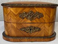 Front view of an antique wooden casket with marquetry veneer, two drawers with ornate gilt metal decorations including a keyhole on the bottom drawer.