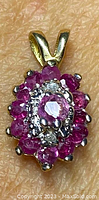 Close-up of the ruby and diamond pendant on textured background showing details of stones and gold setting.