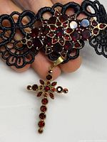 Close-up of black lace collar with garnet gemstones forming a flower cluster and garnet cross hanging pendant