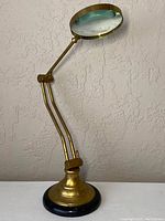 Full view of the antique brass desk magnifying glass with round lens and articulated arm.