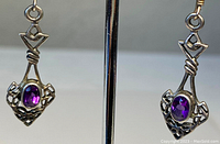 Close-up image of one earring showing sterling silver metalwork with an oval amethyst stone set in the center, featuring the Claddagh design.