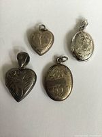 Four antique sterling silver lockets laid out on a white background showing front designs and size comparison.