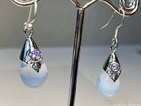 Front view of antique sterling silver moonstone and amethyst teardrop earrings displayed on a metal stand against a neutral background.