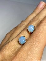 Close-up of both moonstone sterling silver stud earrings on hand, showing the size and blue opalescent sheen of stones.