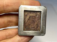 Square silver box held in hand displaying glass top showing an old postage stamp beneath.